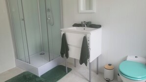 A bathroom with a glass-enclosed shower, a white sink with a mirror above it, and a toilet with a teal lid. - 1Bed Apartment Sleeps 2 - Parking, Wifi (Fougerolles du Plessis)