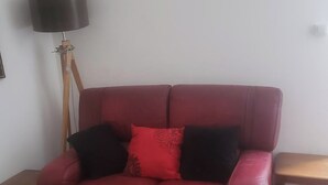 A red leather armchair with a red and black cushion, positioned next to a wooden side table and a floor lamp. - 1Bed Apartment Sleeps 2 - Parking, Wifi (Fougerolles du Plessis)