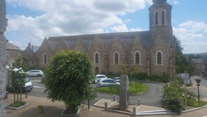 A church with a tall steeple and a clock tower, surrounded by parked cars and greenery. - 1Bed Apartment Sleeps 2 - Parking, Wifi (Fougerolles du Plessis)