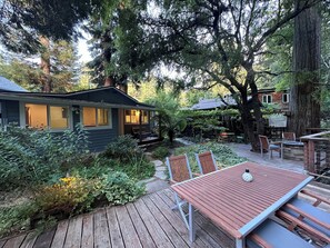 Relax on the deck surrounded by lush greenery and mature trees, with a cozy cabin nearby.