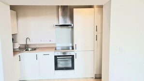 Une cuisine compacte avec des meubles blancs, une hotte en acier inoxydable, un four encastré et un plan de travail en bois.