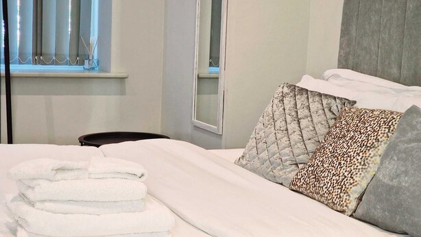 Un lit bien fait, avec des draps blancs et une pile de serviettes pliées.
