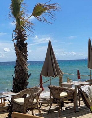 A beachside patio with wicker furniture and umbrellas, overlooking the ocean. - Loue Villa 8 Couchages à 3mm à Pied de la Plage,piscine,climatisé,cavalaire/mer (Cavalaire-sur-Mer)