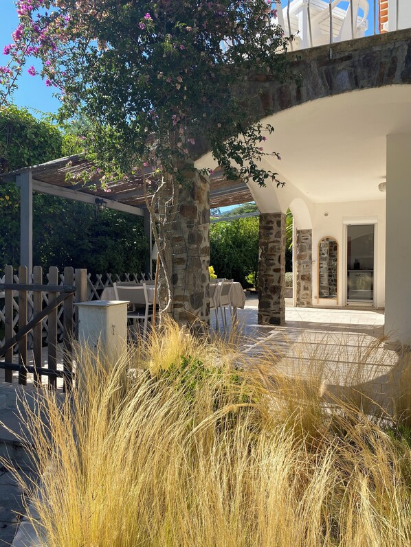 A covered outdoor seating area with stone pillars, a pergola, and a view of the property. - Loue Villa 8 Couchages à 3mm à Pied de la Plage,piscine,climatisé,cavalaire/mer (Cavalaire-sur-Mer)