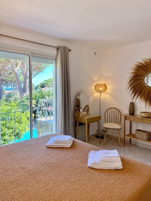 A bedroom with a large window, a bed with folded towels, a chair, a desk, a lamp, and a mirror. - Loue Villa 8 Couchages à 3mm à Pied de la Plage,piscine,climatisé,cavalaire/mer (Cavalaire-sur-Mer)