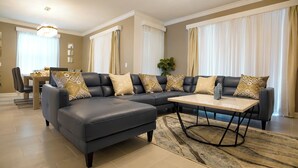 Una sala moderna con un sofá modular, una mesa de centro y un comedor al fondo.