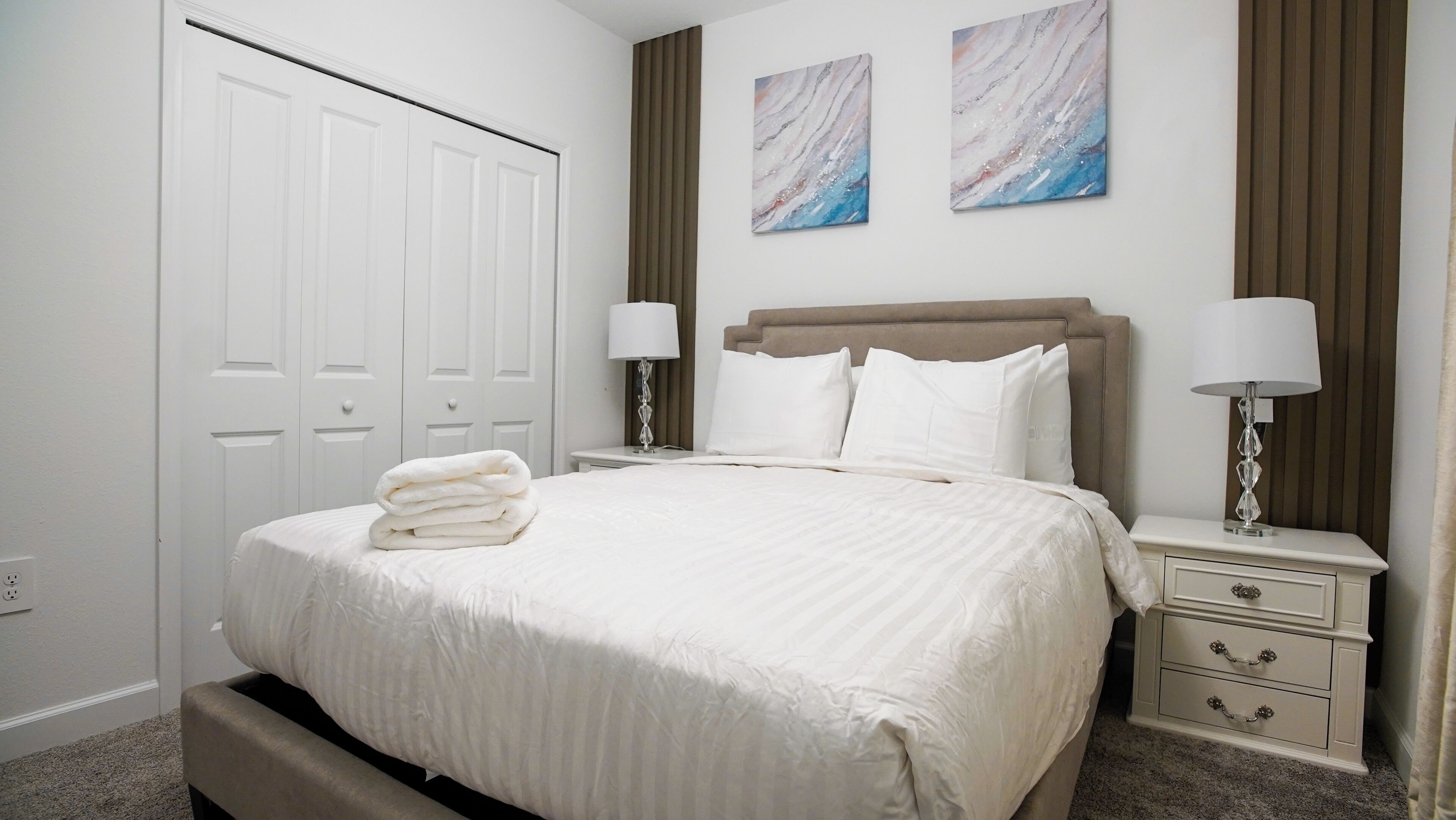 A hotel room with a large bed, two bedside tables with lamps, a headboard, and a wardrobe.