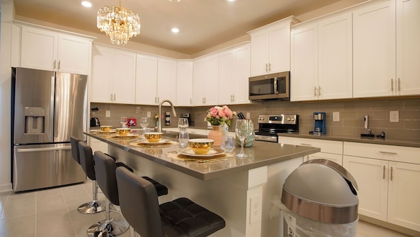 Una cocina moderna con armarios blancos, electrodomésticos de acero inoxidable, una isla central con asientos y una lámpara de araña.