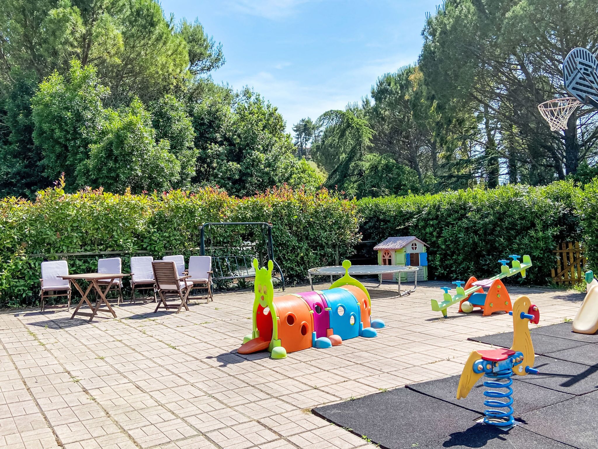 A playground with various play structures, a small house, and seating area with chairs and tables.