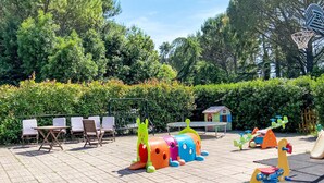 Un parque infantil con diversas estructuras de juego, una casita y una zona de estar con sillas y mesas.