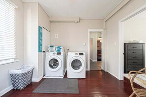 A laundry room with two washing machines, a drying rack, a trash bin, and a door leading to another room. - Speakeasy, Hot tub, 1920s Family Beach Home (Atlantic City)