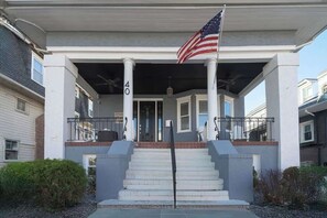 A two-story residential building with a covered front porch, a flagpole with an American flag, and a staircase leading to the entrance. - Speakeasy, Hot tub, 1920s Family Beach Home (Atlantic City)