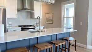 Una cocina moderna con una isla grande, taburetes de bar, electrodomésticos de acero inoxidable y un ventanal que proporciona luz natural.