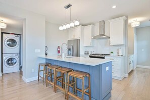 A modern kitchen with a central island, bar stools, a washing machine, and a built-in oven.