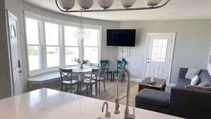 Cocina moderna con una isla grande, comedor con mesa y sillas, televisor de pantalla plana en la pared y zona de estar con sofá.
