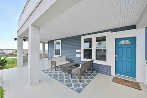 A covered porch with a blue door, white walls, and a patterned rug.