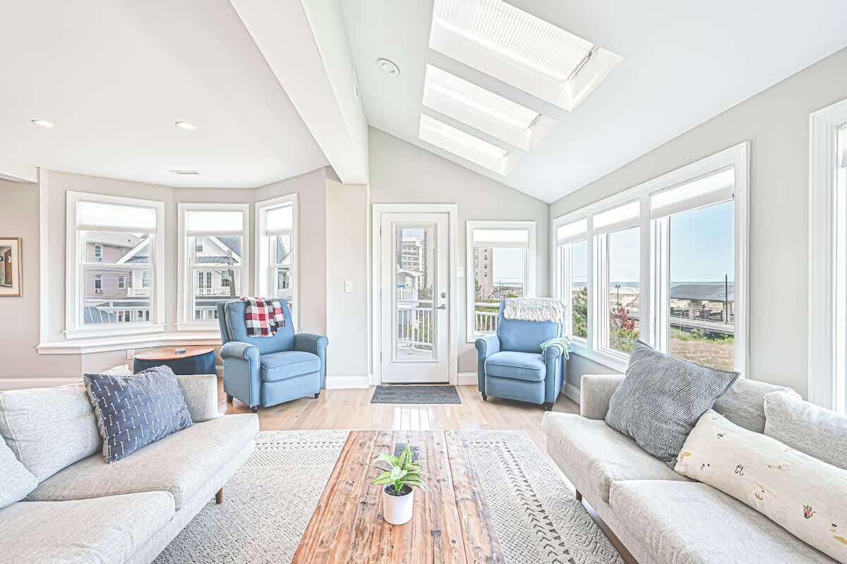 A spacious living room with large windows, a wooden coffee table, and two blue armchairs.