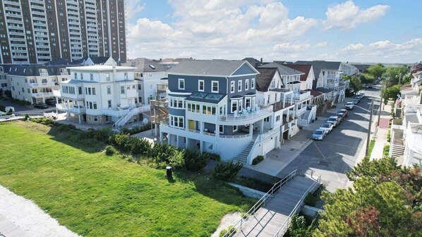 A residential area with multi-story houses, a grassy lawn, and a street with parked cars.