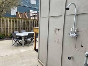 Eine Terrasse im Freien mit Tisch und Stühlen, einem Holzzaun und einer grauen Wand mit einer Duschbrause.