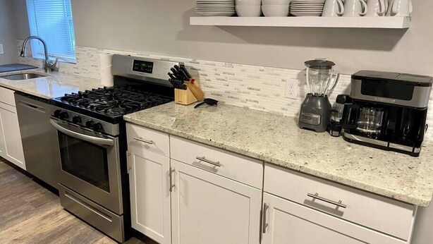 A kitchen with white cabinets, a stainless steel stove, a coffee maker, and a blender on the countertop. - Beach Tower boardwalk walkout (Atlantic City)