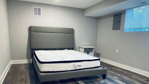 A bedroom with a bed, a nightstand, a window, and a wall vent. - Beach Tower boardwalk walkout (Atlantic City)