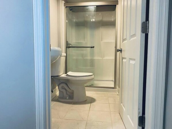 A bathroom with a toilet, a glass shower enclosure, and a white door. - Beach Tower boardwalk walkout (Atlantic City)