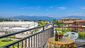 Ein Balkon mit Tisch, einer Flasche und einem Stuhl mit Blick auf eine Stadtlandschaft, Gebäude und eine entfernte Bergkette.