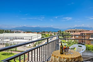 Un balcón con una mesa, una botella y una silla con vistas a un paisaje urbano que incluye edificios y una cadena montañosa distante.