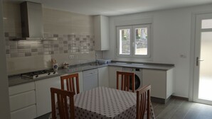 A modern kitchen with white cabinets, a gas stove, a dishwasher, and a window with a view of greenery. - House in Lira near the beach (Sofan (Santa Maria De Lira-Carnota))