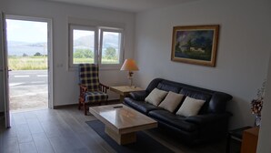 A living room with a black leather sofa, a wooden coffee table, a checkered armchair, a small table with a lamp, and a painting on the wall. - House in Lira near the beach (Sofan (Santa Maria De Lira-Carnota))