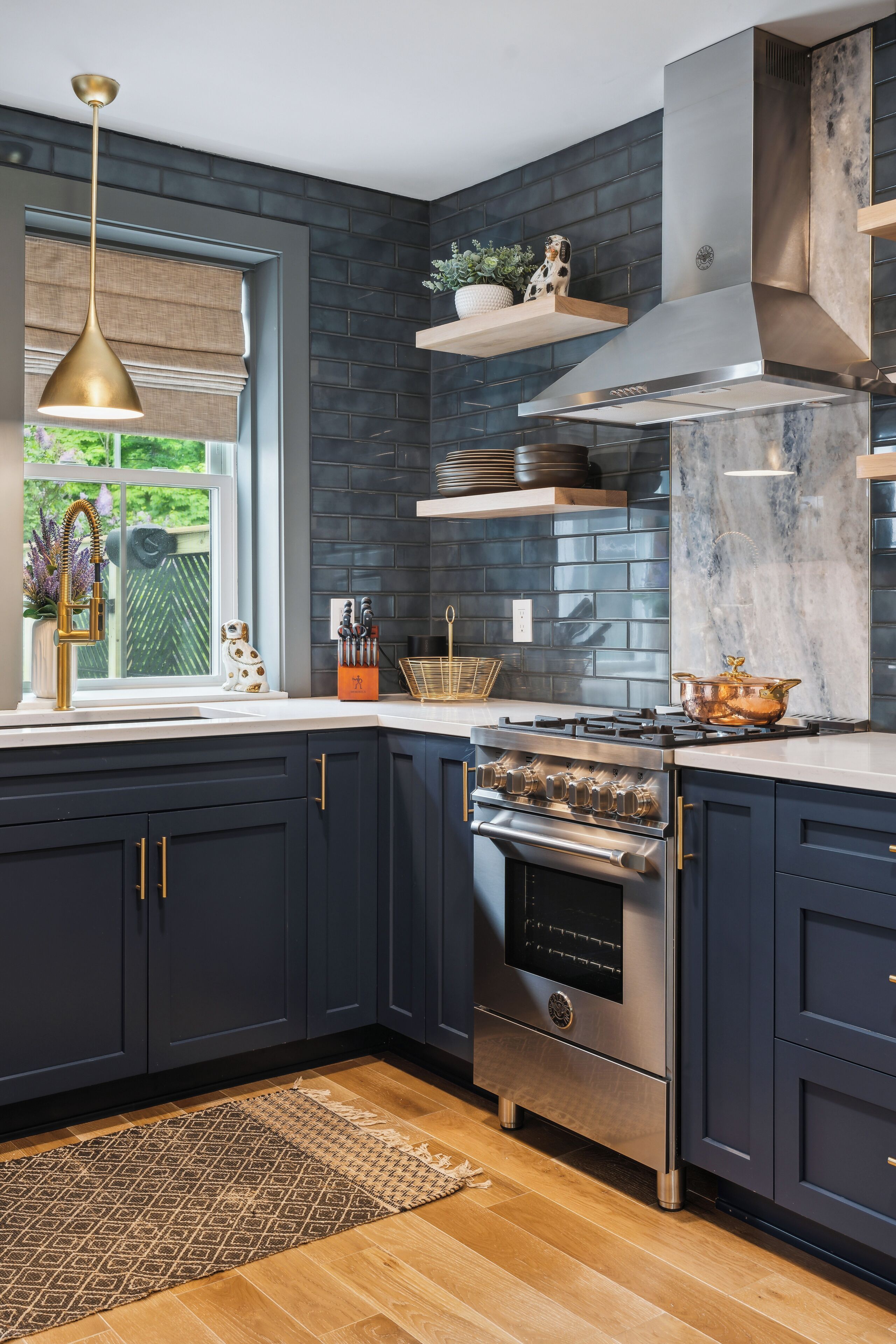 A modern kitchen with dark cabinetry, a stainless steel range, and a window with a view of greenery.