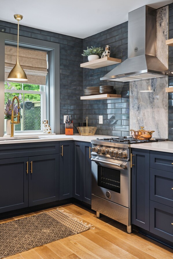 A modern kitchen with dark cabinetry, a stainless steel range, and a window with a view of greenery.