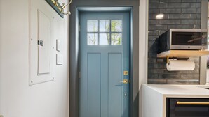 A blue door with a window, a wall-mounted light switch, and a microwave on a counter.