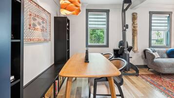 Uma sala de estar moderna com uma mesa de jantar de madeira, um sofá cinza, um tapete estampado e uma grande janela com persianas.