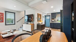 A modern kitchen with dark cabinetry, a wooden dining table, and a staircase leading to another level.