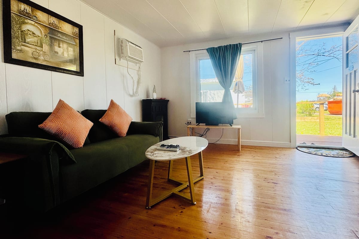 A living room with a green sofa, a small white table, a television, and a window with curtains.