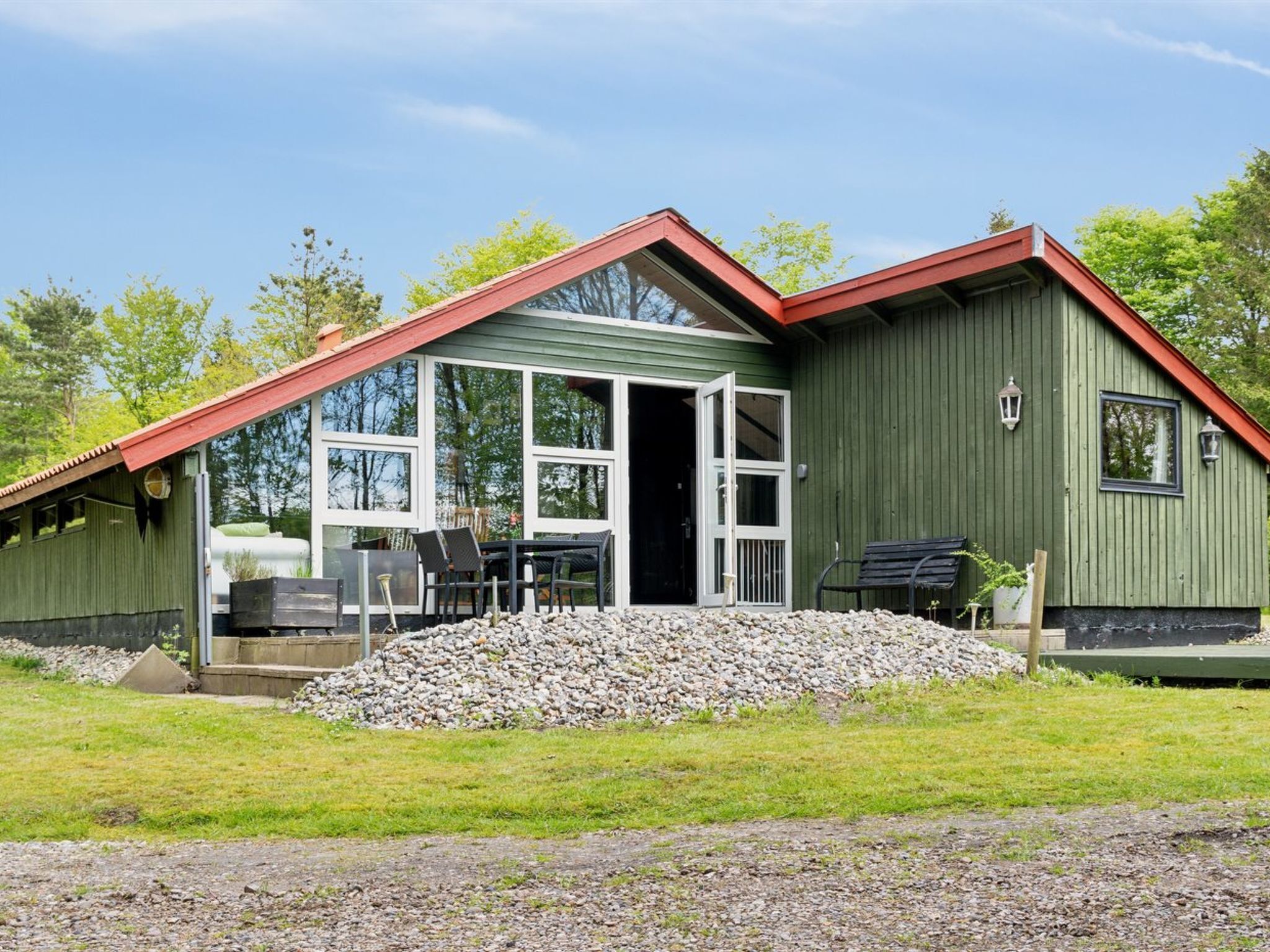 A green building with a red roof, large windows, and a patio area with outdoor furniture.