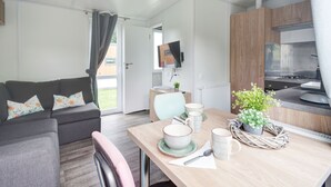 En moderne og lys stue med en grå sofa, et spisebord med keramikservice og et køkken med træskabe og en komfur.