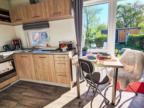 A modern kitchen with wooden cabinets, a dining table with chairs, and a view of the outdoors. - Tiny Haus Heidi by Interhome (Beilngries)