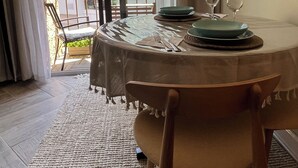 Un coin repas avec une table ronde dressée pour deux personnes, une vue sur un balcon et un bâtiment en arrière-plan.