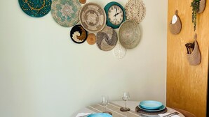 Un coin repas avec une table ronde dressée pour deux personnes, agrémenté d’une nappe à rayures et d’une horloge au mur.