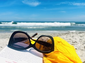 A pair of sunglasses and a book on a beach with ocean waves in the background.