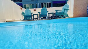 Une piscine à l’eau bleue, entourée de murs blancs, avec un bâtiment aux grandes fenêtres en arrière-plan.