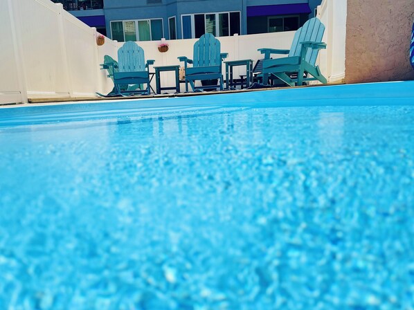 A swimming pool with blue water, surrounded by white walls and a building with large windows in the background.