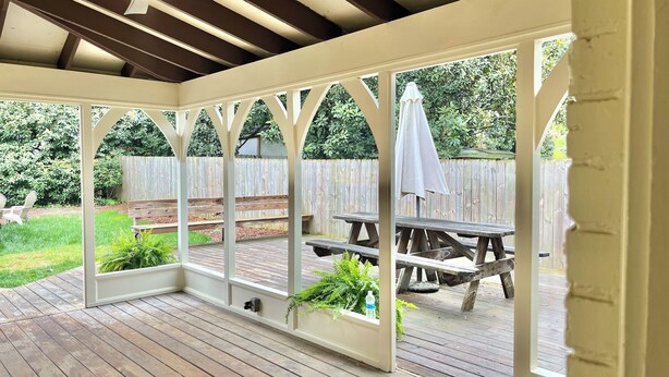 Ein überdachter Patio-Bereich mit Holzboden, weißen Geländern und einem Holztisch mit Bänken.