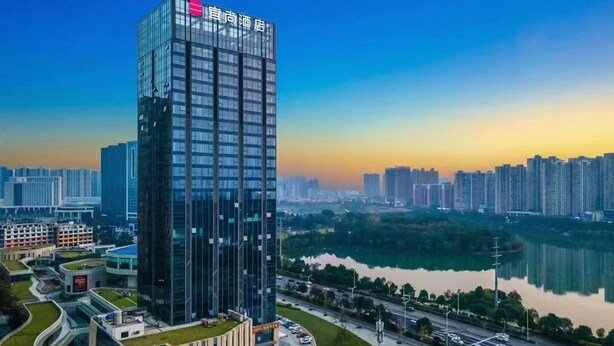 A modern high-rise hotel with a glass facade, surrounded by a cityscape and a body of water. - Yishang Hotel (Changsha)