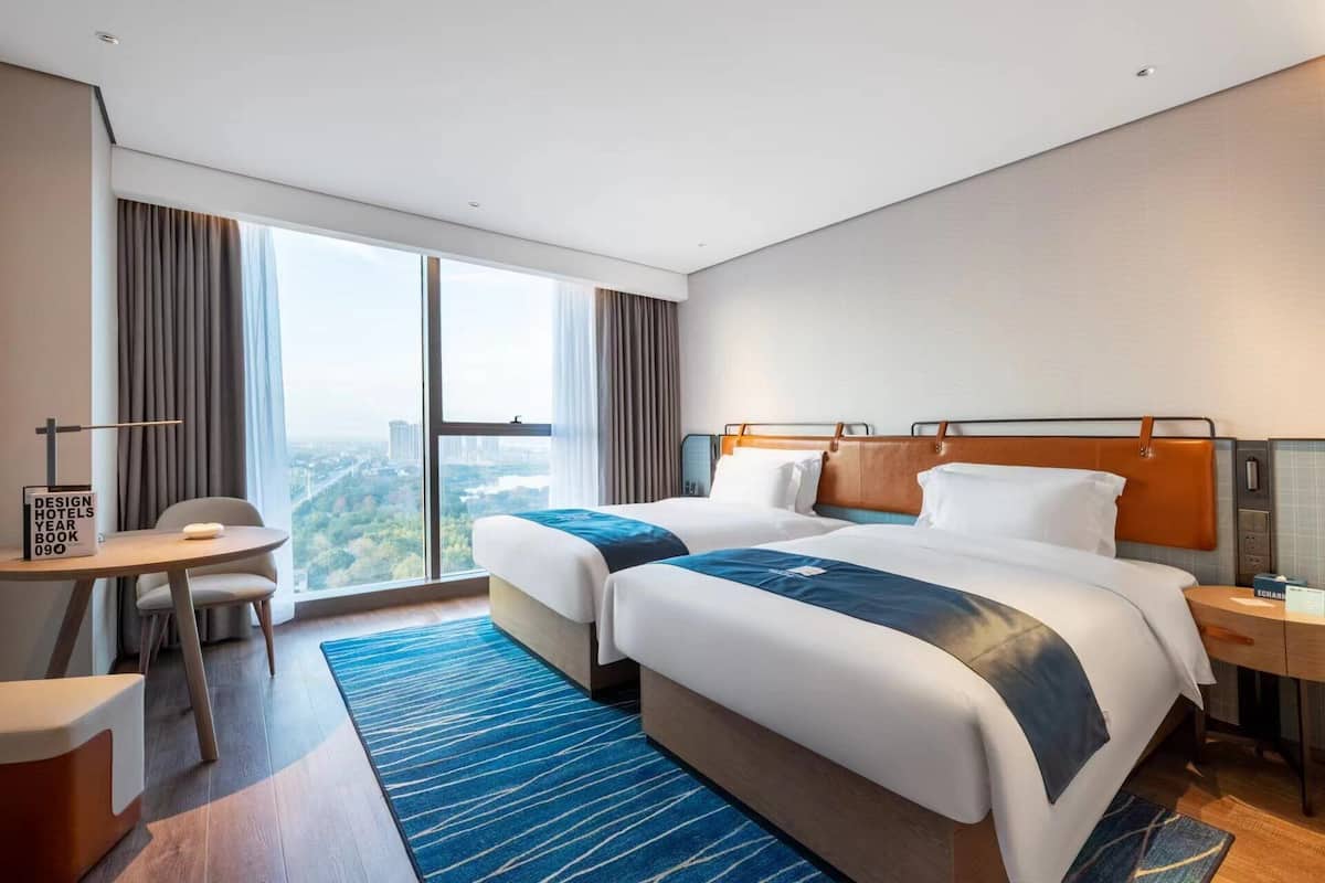 A hotel room with two beds, a desk, and a view of the city.