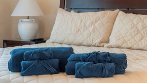 A neatly made bed with a quilted headboard, a bedside lamp, and several folded towels. - Davenport Andros Condo Retreat (Davenport)