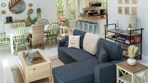 Un salón amplio con techo alto, una escalera de madera y una cocina al fondo.