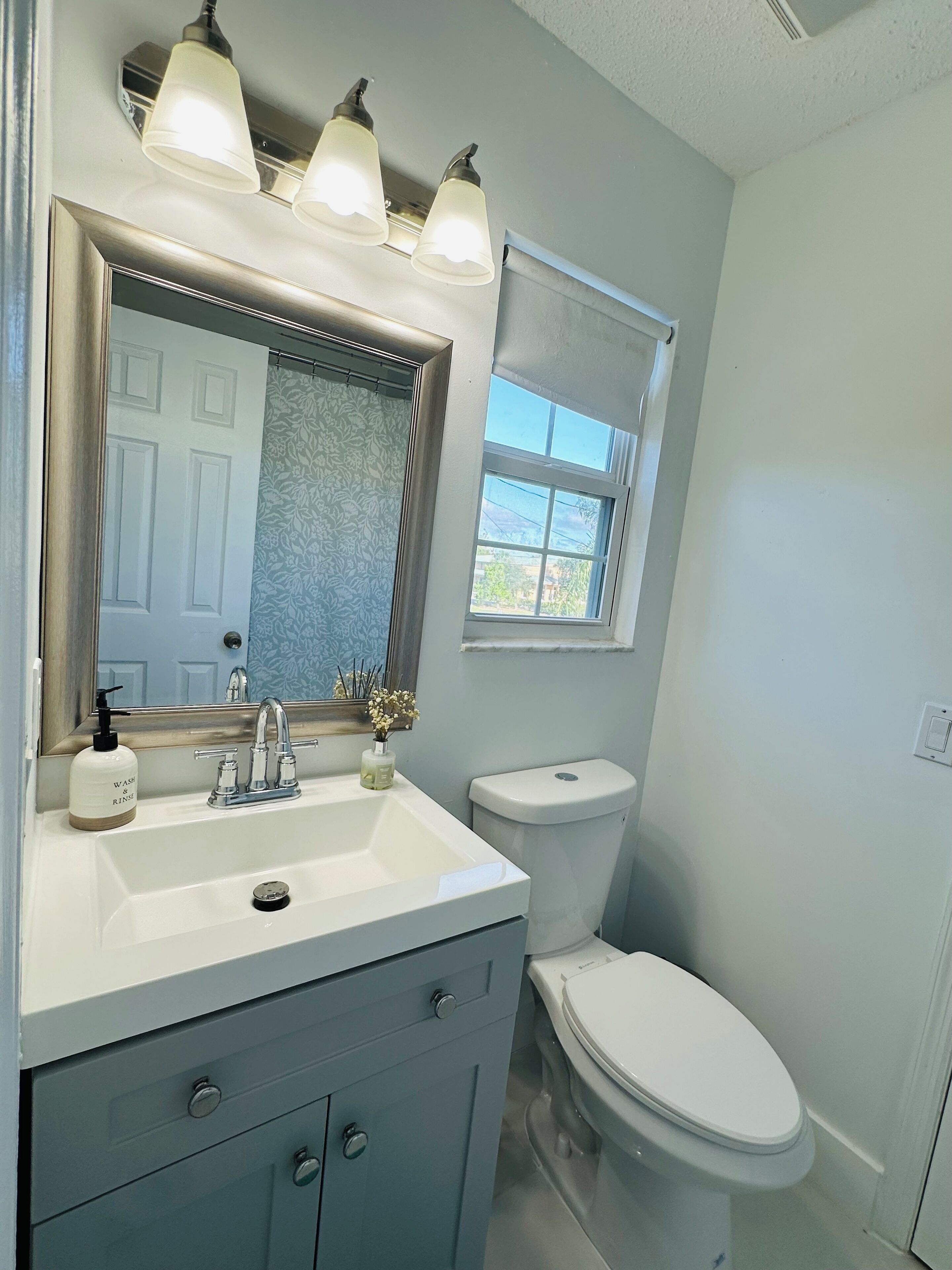 Une salle de bain avec un lavabo blanc, un miroir, des toilettes et une fenêtre.